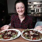 Doris sitzt mit ausgebreiteten Armen vor 2 Pizzen im Rohkostrestaurant Rawtastic in Berlin.